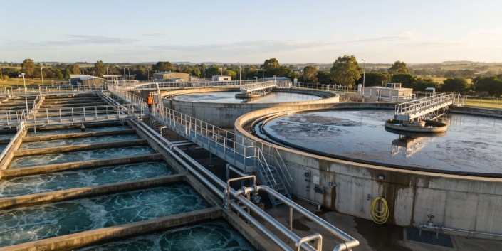Hydroflux Case Study Hero: Wastewater Treatment Plant Elevated view of a municipal wastewater treatment plant with circular clarifier tanks and aeration basins at golden hour